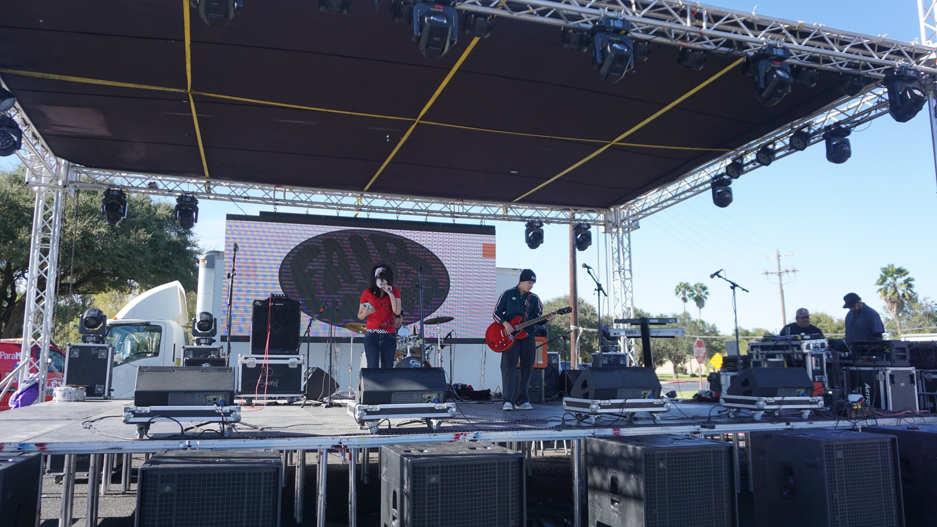 A singer and guitarist perform on the festival stage with a drum kit and a large backdrop behind them.