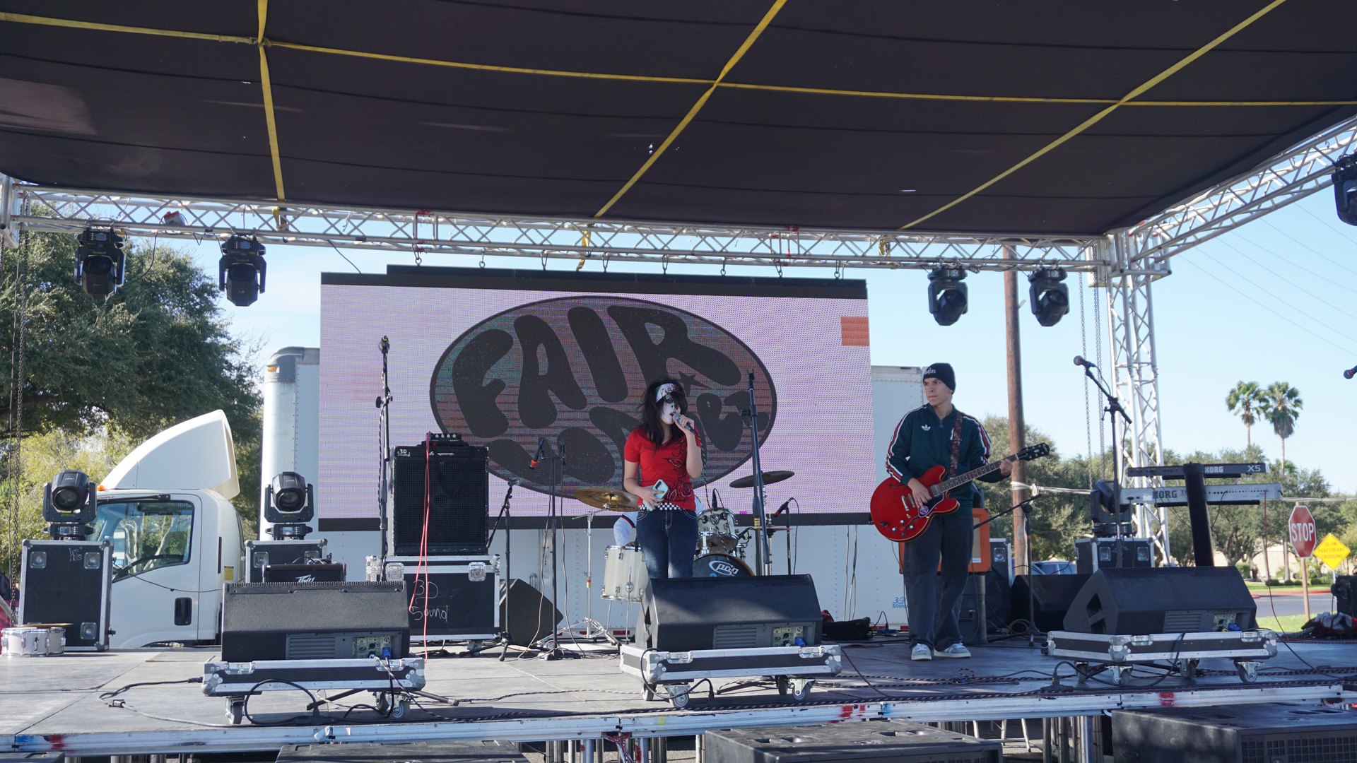 A singer performs beside a musician playing a red electric guitar on the covered festival stage.