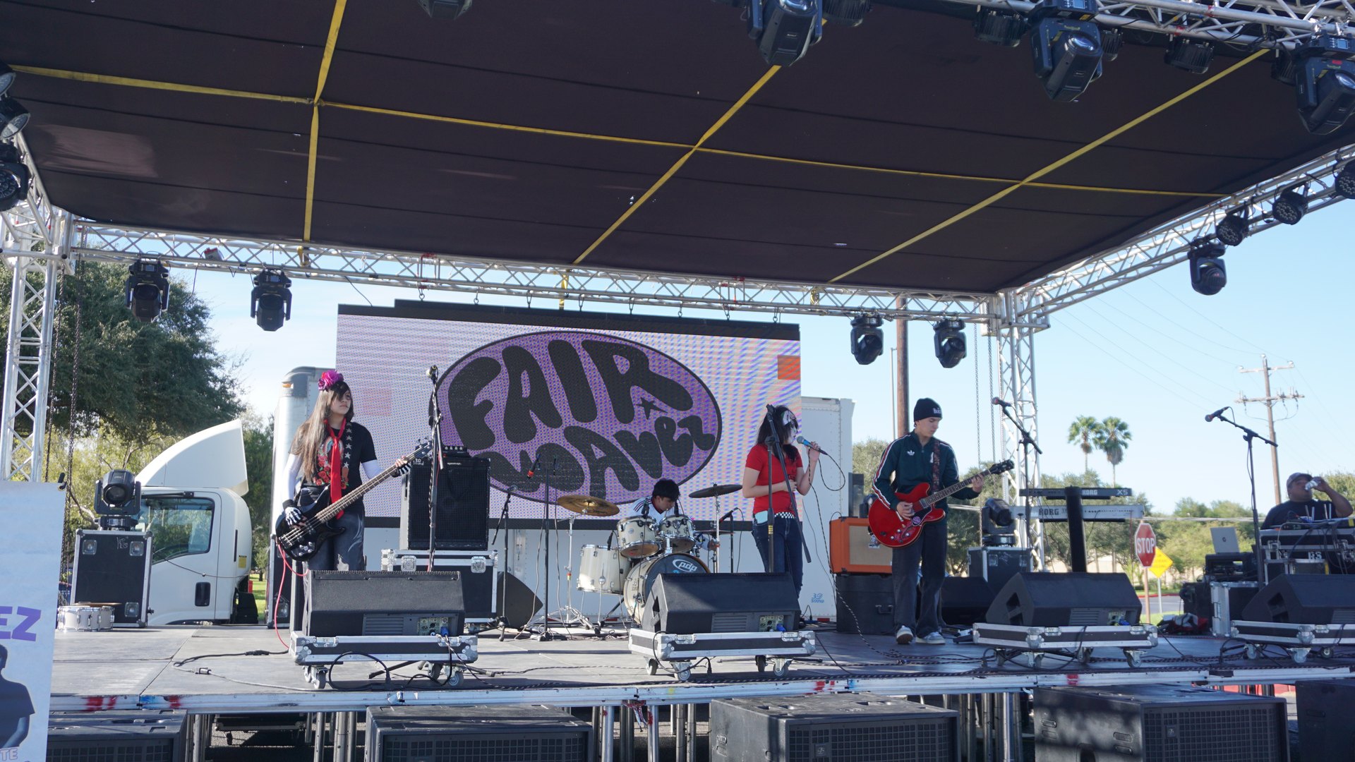 Musicians perform across the outdoor festival stage beneath a dark canopy.