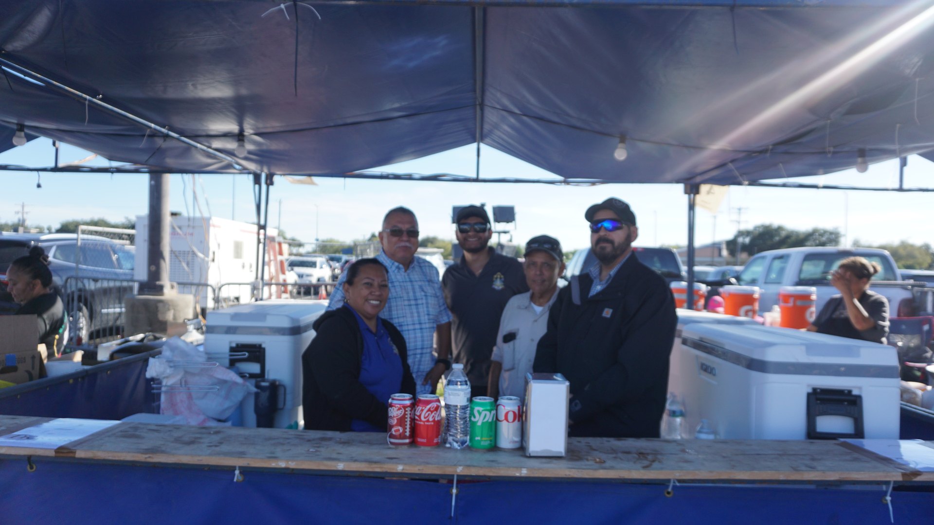 A smiling concession team gathers behind a food booth counter under a canopy.