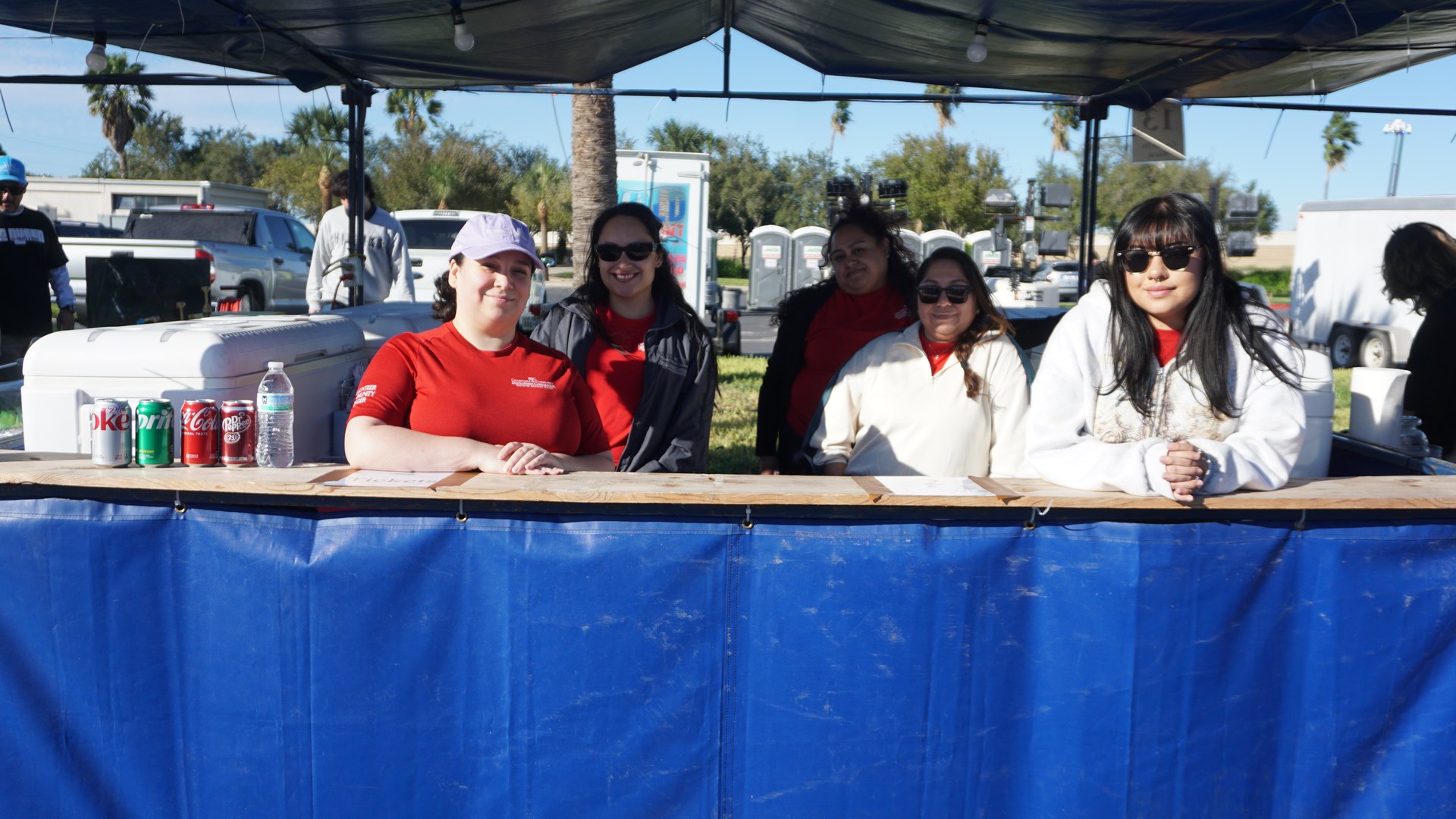 A concession team poses behind a wide blue booth counter beneath a dark canopy.