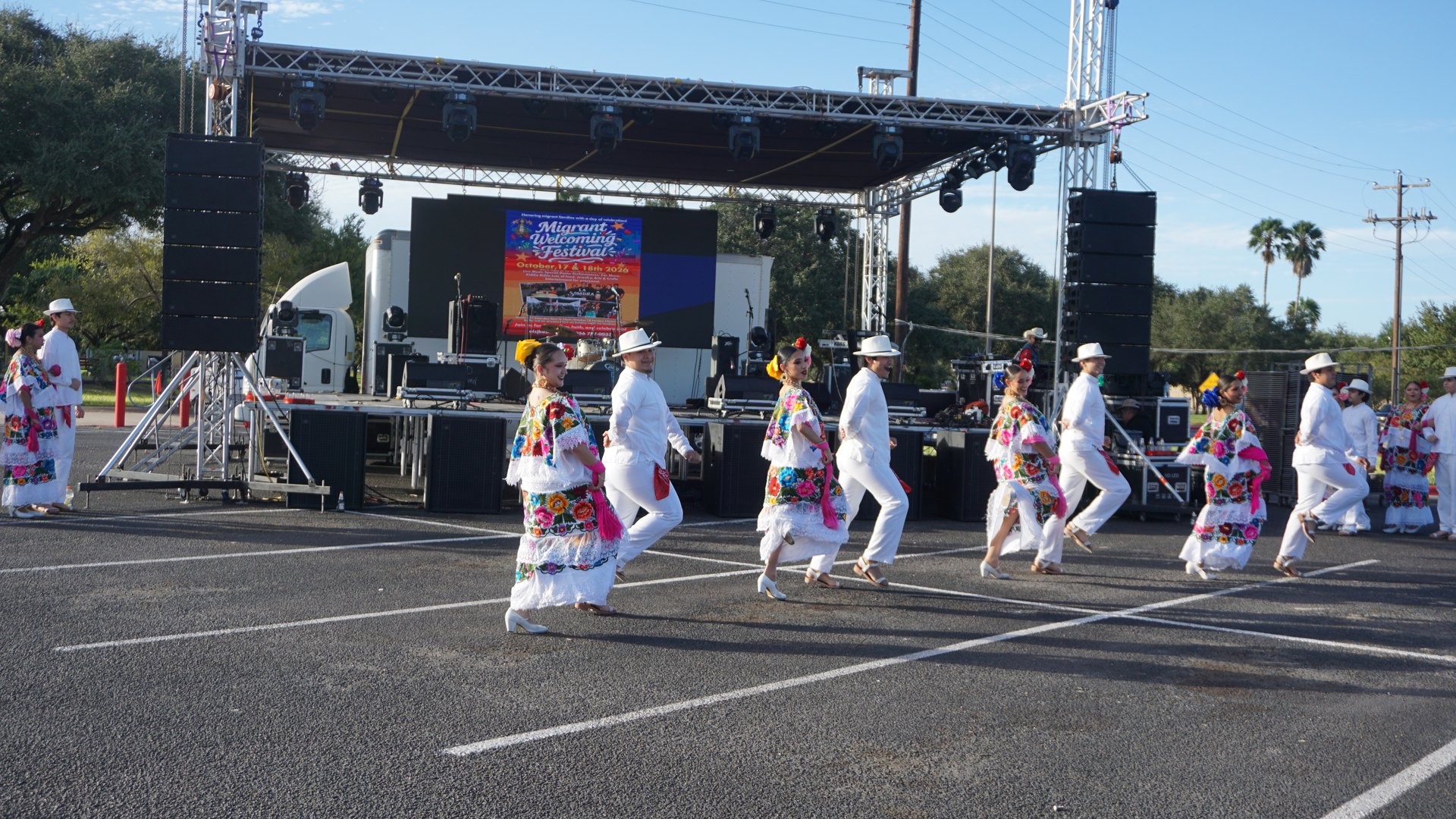 Dancers in white outfits and brightly embroidered dresses perform in front of the festival stage.