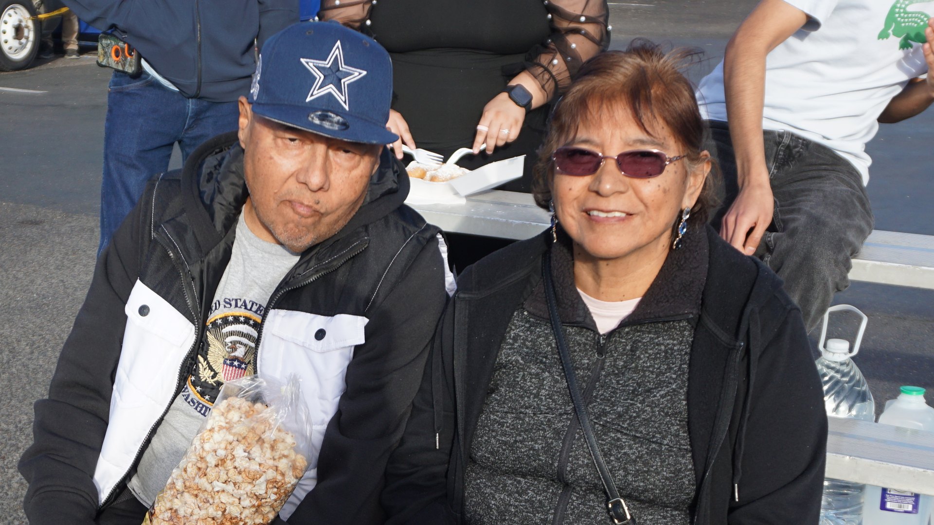 Close view of two guests seated on bleachers, one holding a large bag of popcorn.