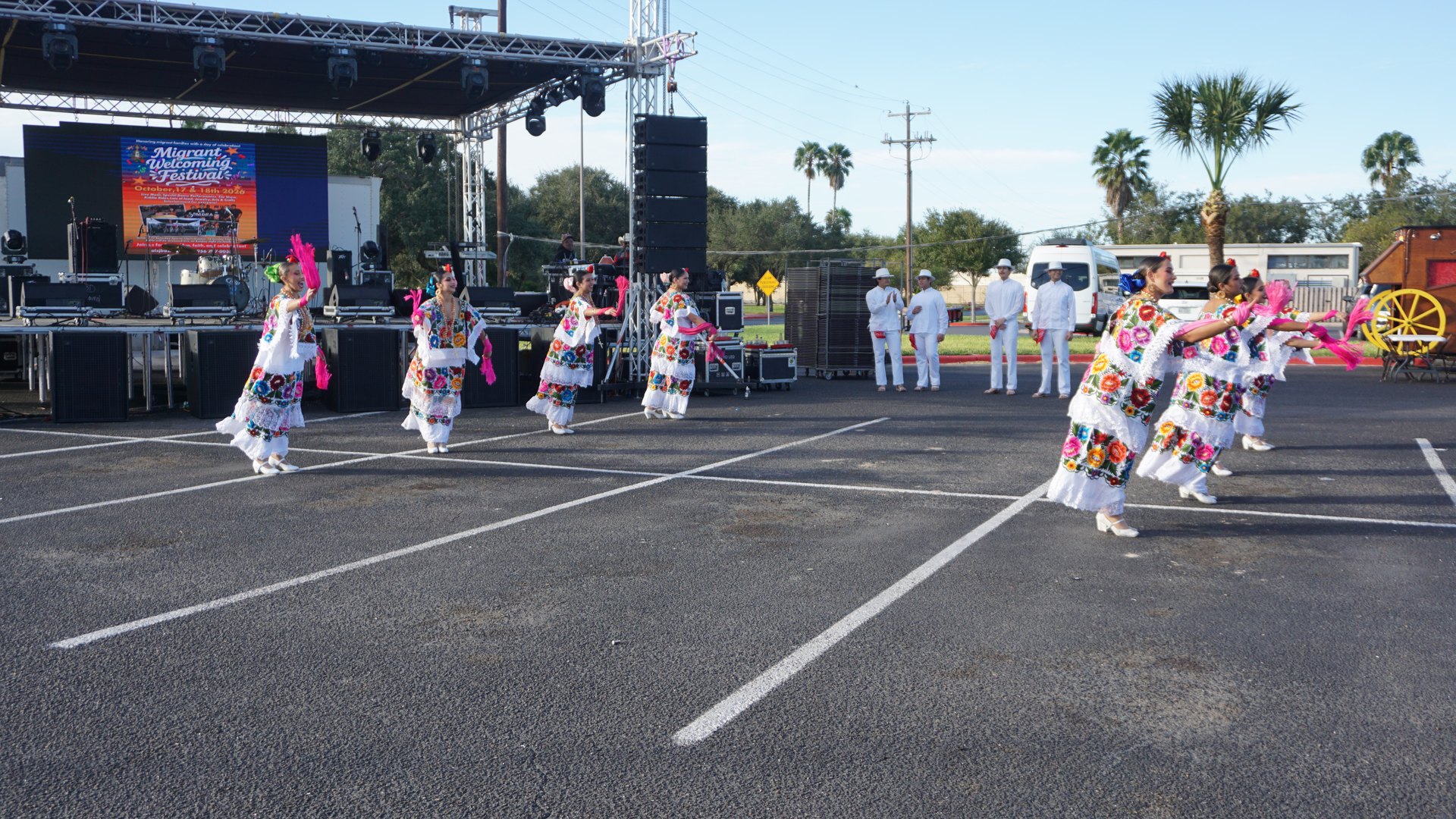 Pairs of dancers step across the performance area in front of the festival stage.