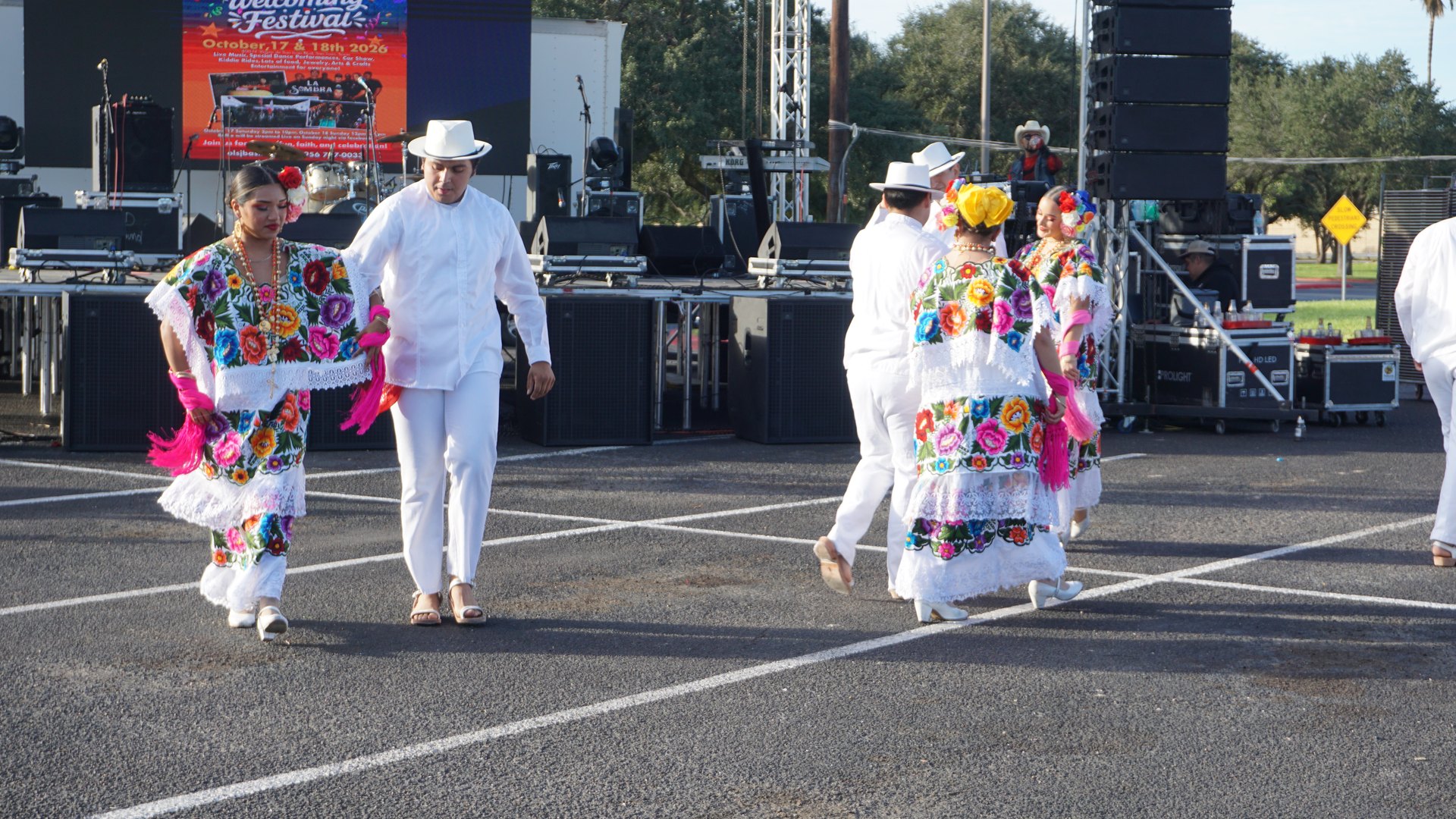 Dancers in floral embroidered dresses and white suits perform close to the festival stage.