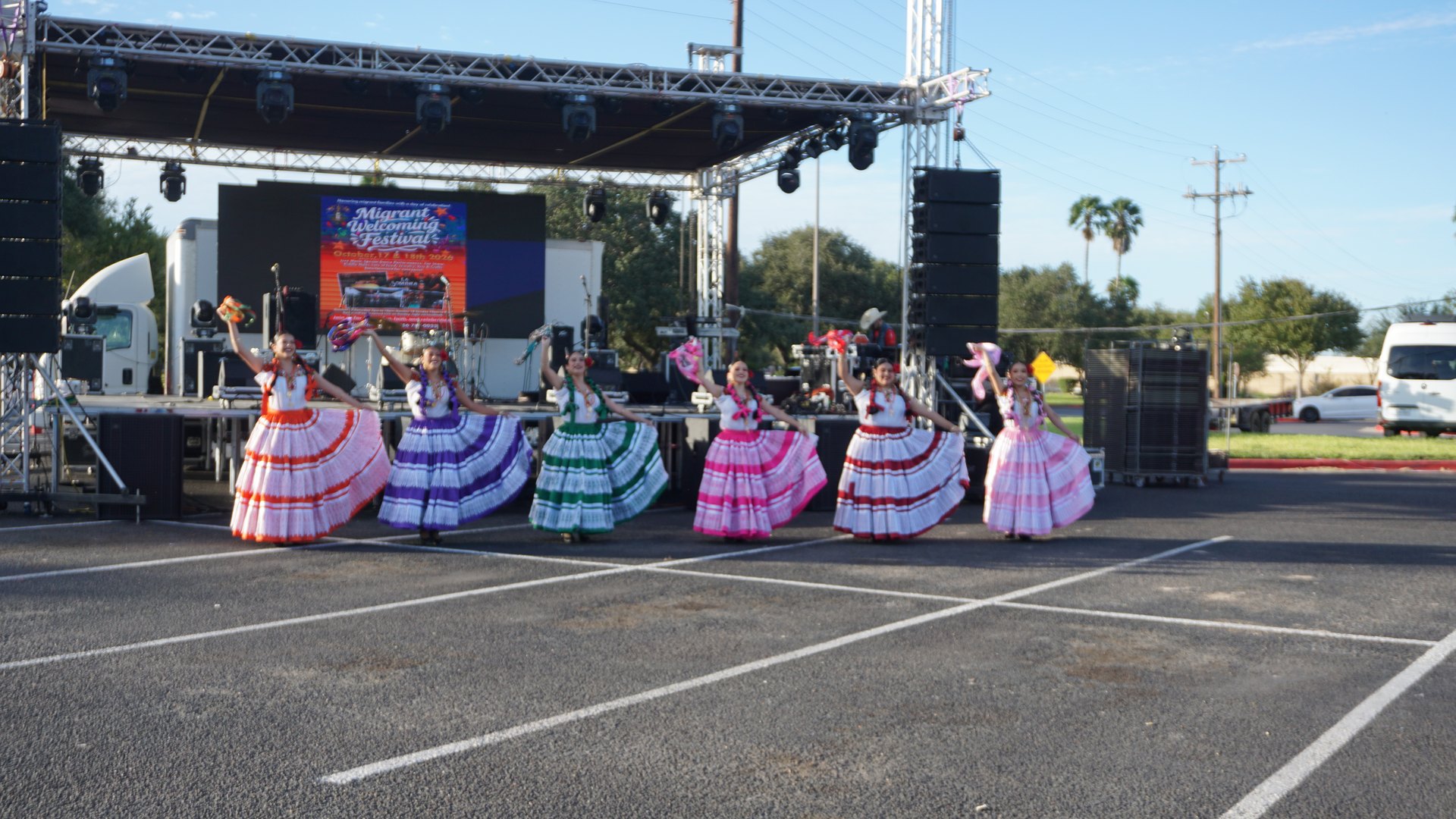 Dancers in colorful tiered dresses line up in front of the festival stage.