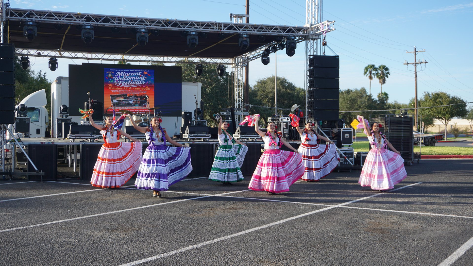 Dancers raise bright handkerchiefs while wearing multicolored ribbon-trimmed dresses.
