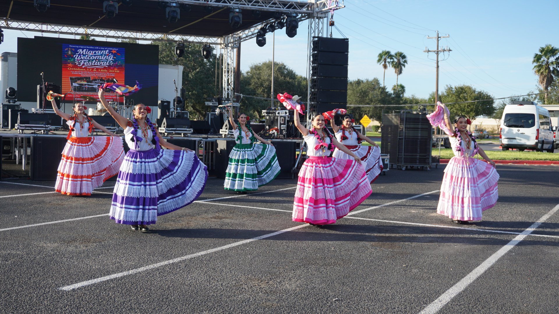 Smiling dancers wave colorful handkerchiefs and display their full skirts in front of the festival stage.
