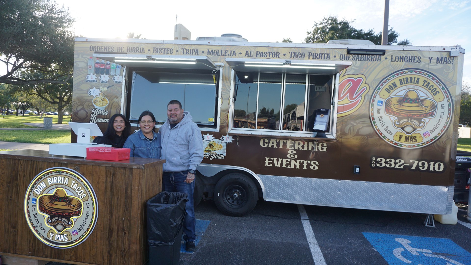 Three food vendors pose beside their counter in front of the Don Birria Tacos trailer.