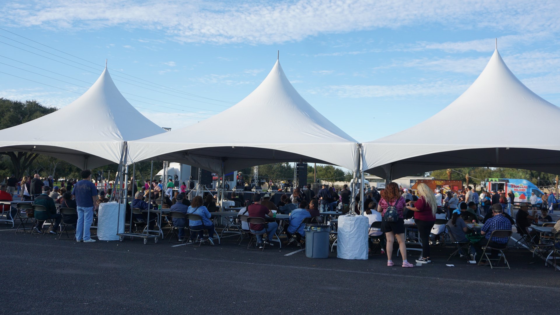 Festival guests gather around tables beneath three large white peaked tents.