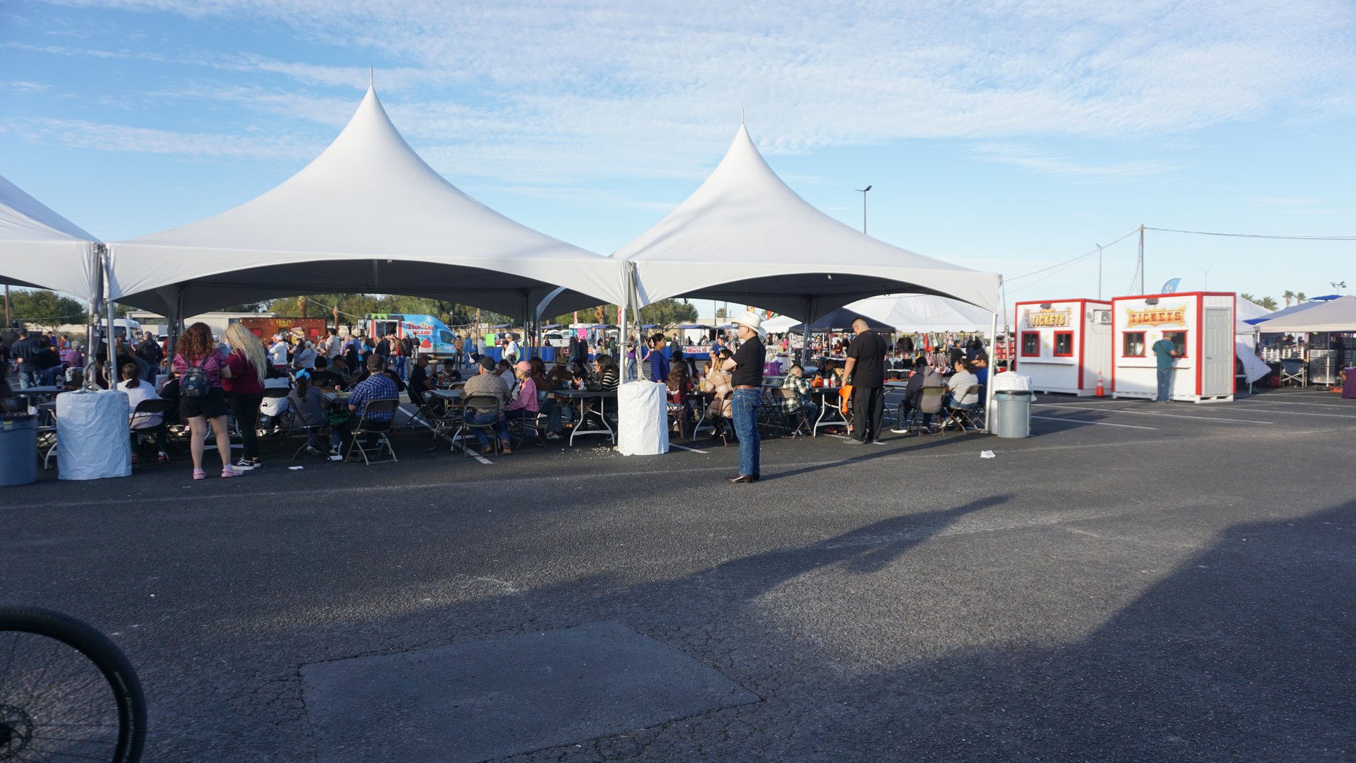 Wide view of festival guests seated beneath white tents, with food trucks nearby.