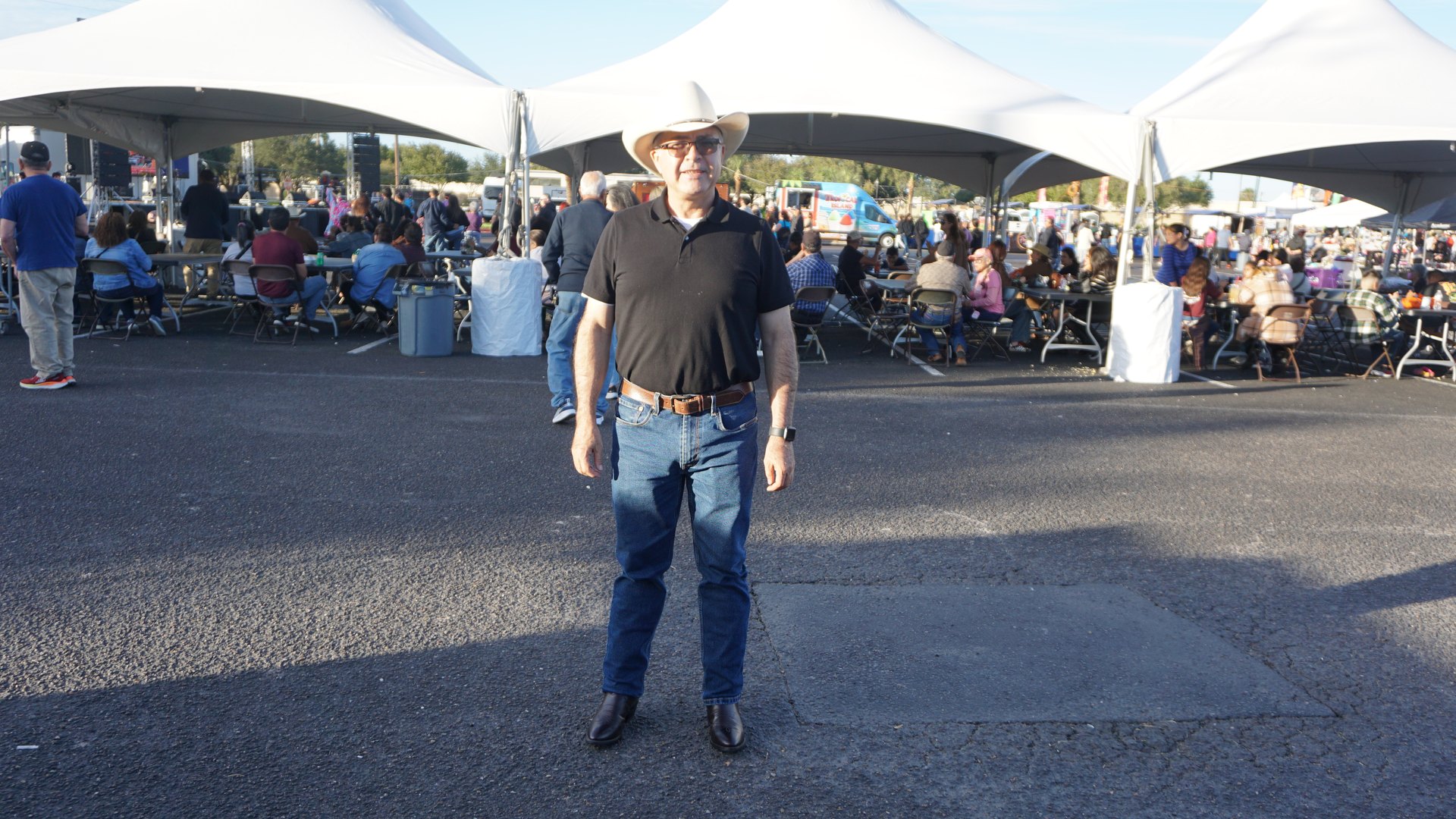 A guest wearing a cowboy hat poses in front of the festival dining tents.