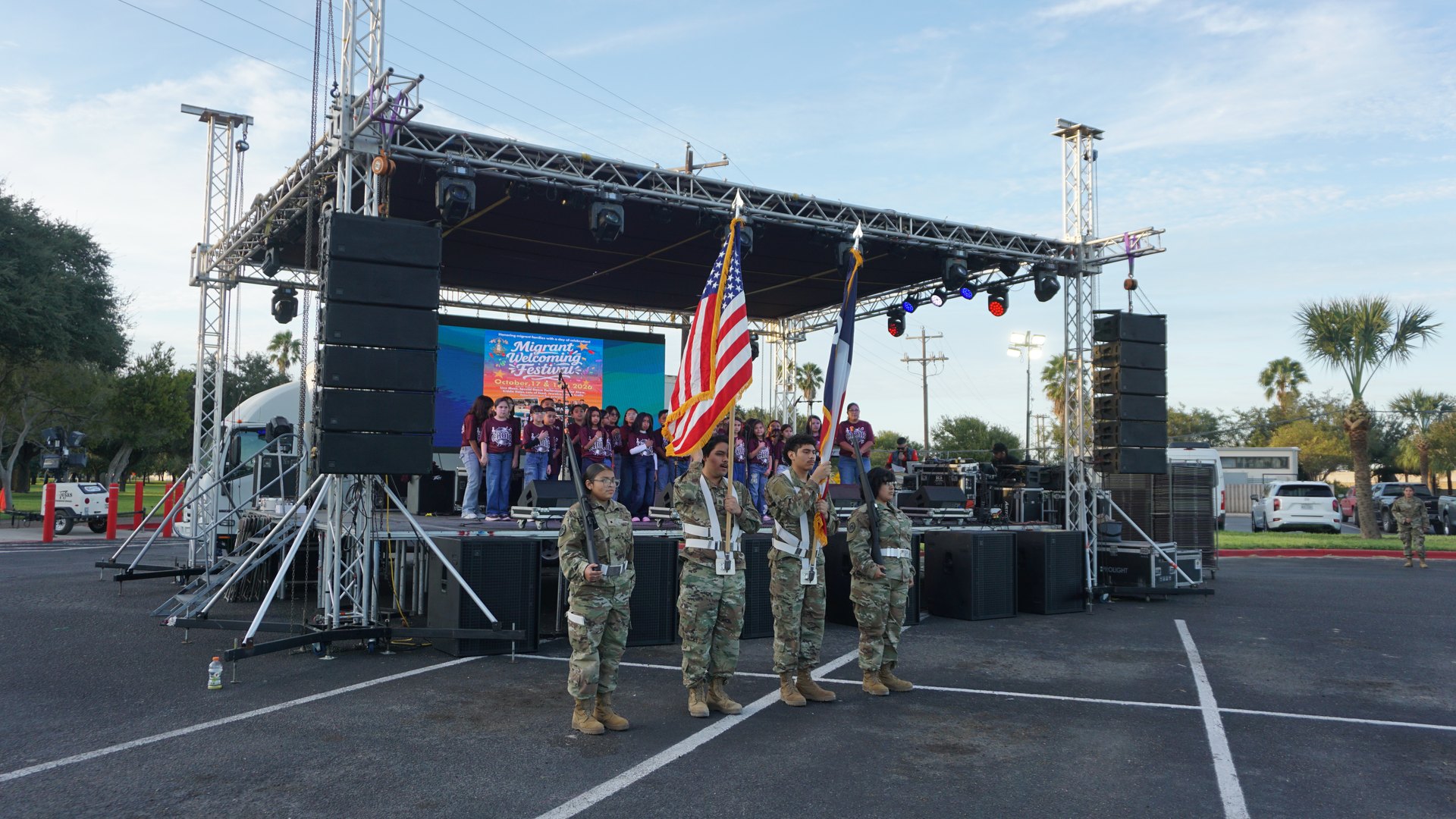 Four uniformed participants carry flags in front of the stage while the choir stands behind them.