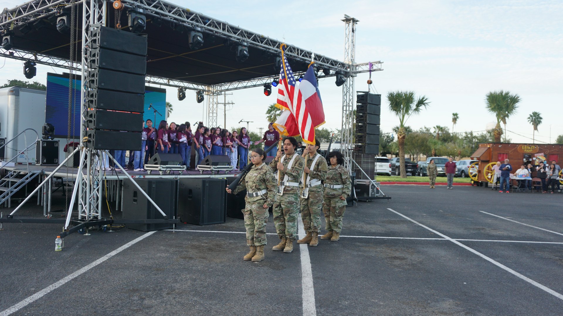 Four uniformed participants stand with flags as the choir gathers on the festival stage.