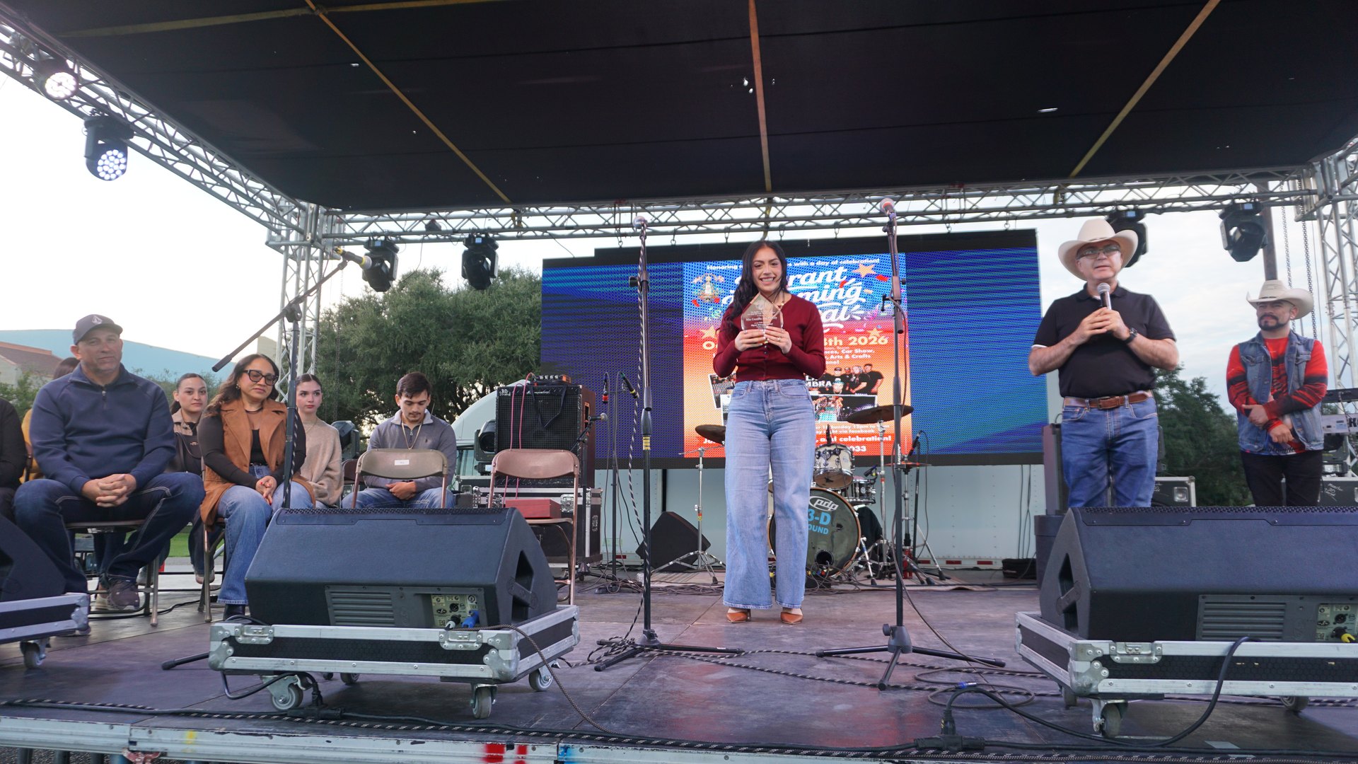 A young woman and a man in a cowboy hat speak onstage during the festival presentation.