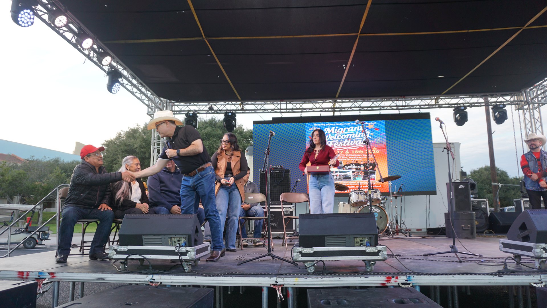 People on the festival stage exchange greetings during a presentation beside the microphones.