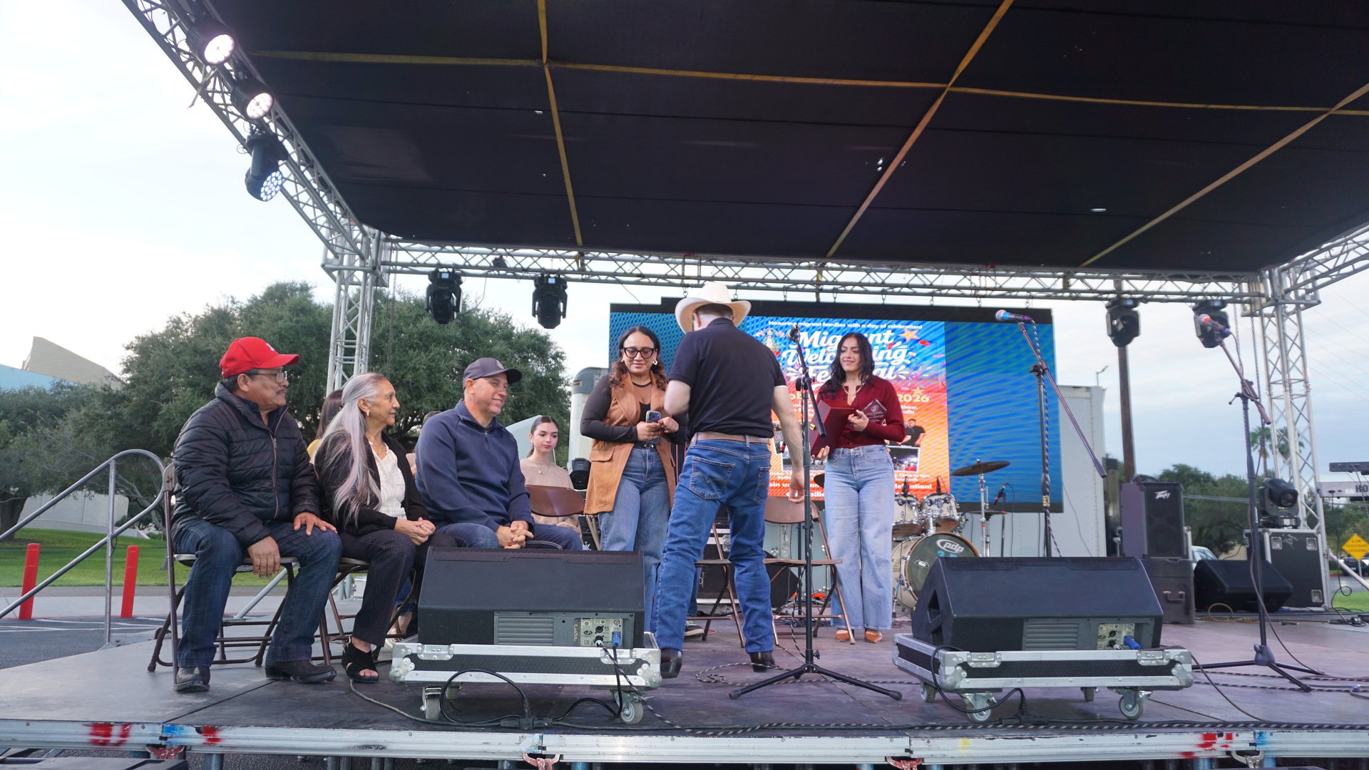A woman stands to greet a man in a cowboy hat as other guests watch from their seats onstage.