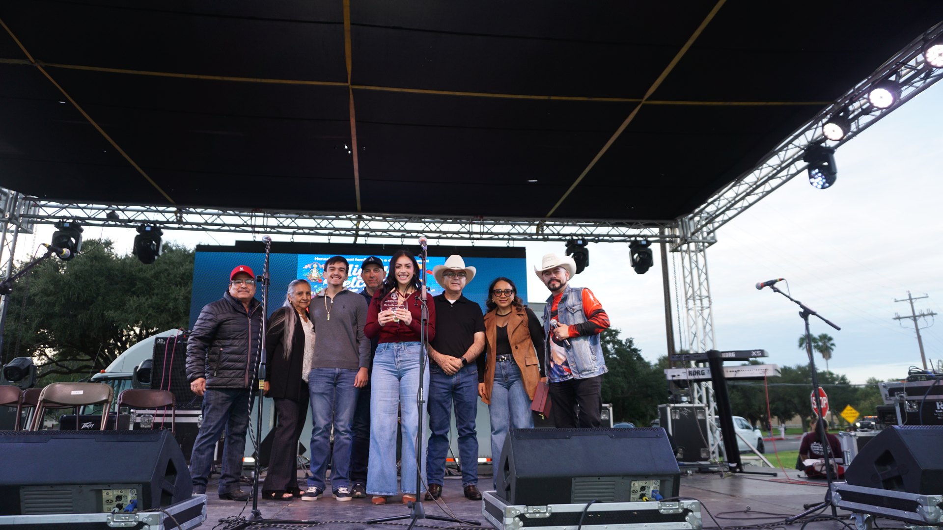 A group poses together on the festival stage in front of the event sign and musical instruments.