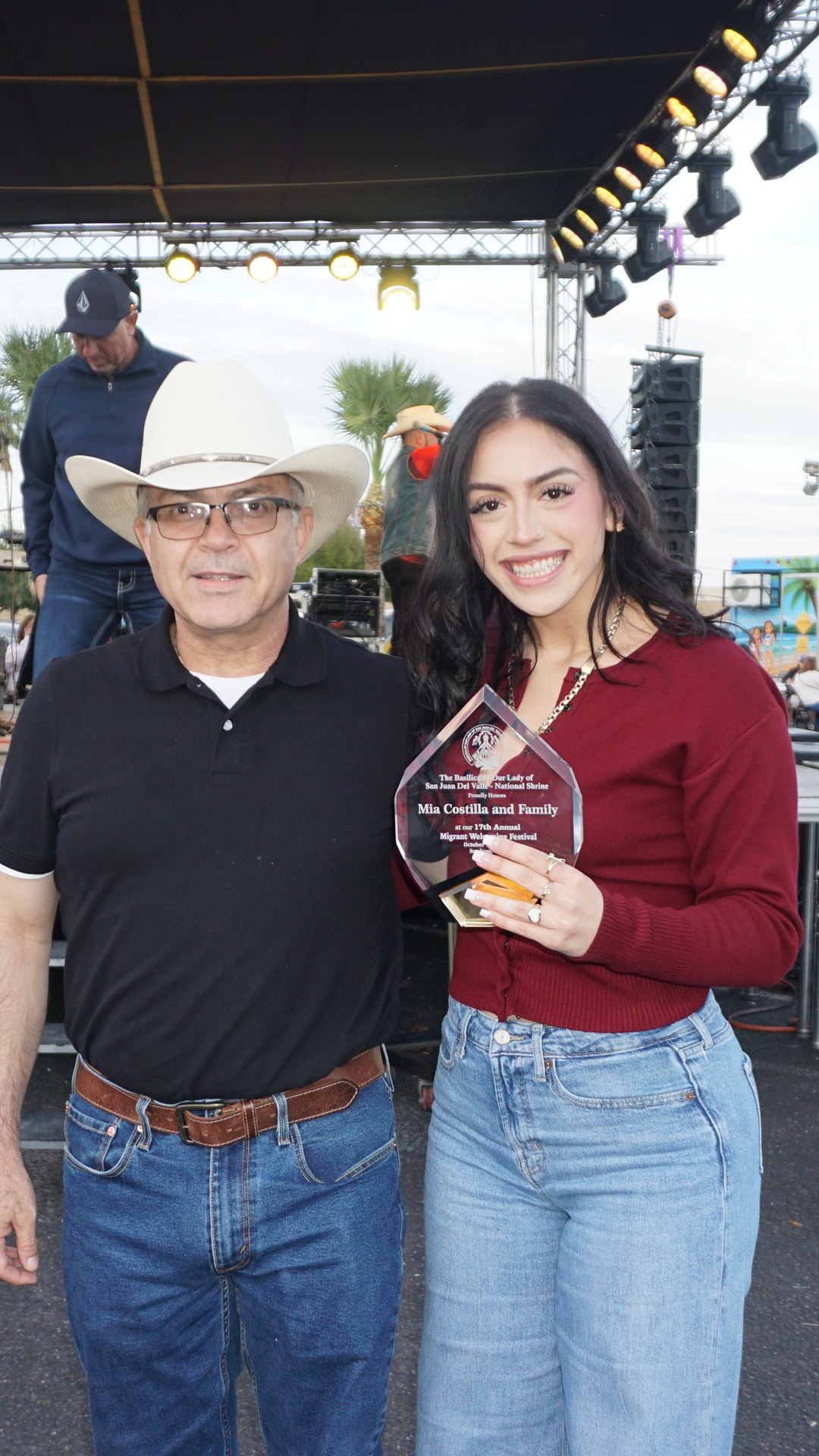A portrait of a young woman holding a plaque beside a man in a white cowboy hat at the festival.