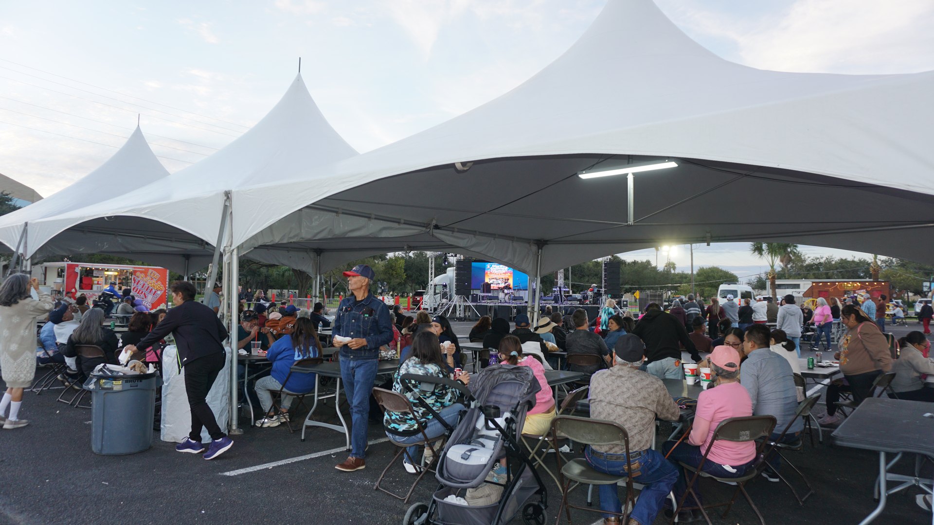 People share food and conversation at tables under white tents as evening approaches at the festival.